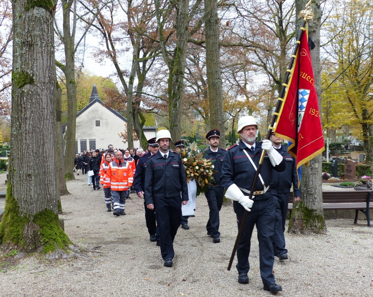 Feuerwehr, DRK und Besucher*innen auf dem Weg zum Ehrenmal auf dem Friedhof.