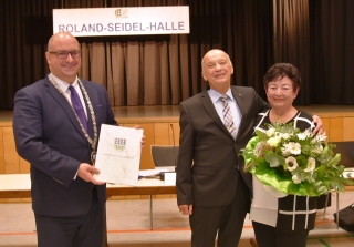Bürgermeister Jens Geiß überreicht die Urkunde zum Ausscheiden aus dem Gemeinderat an Roland Seidel, Gisela Seidel erhält einen Blumenstrauß.