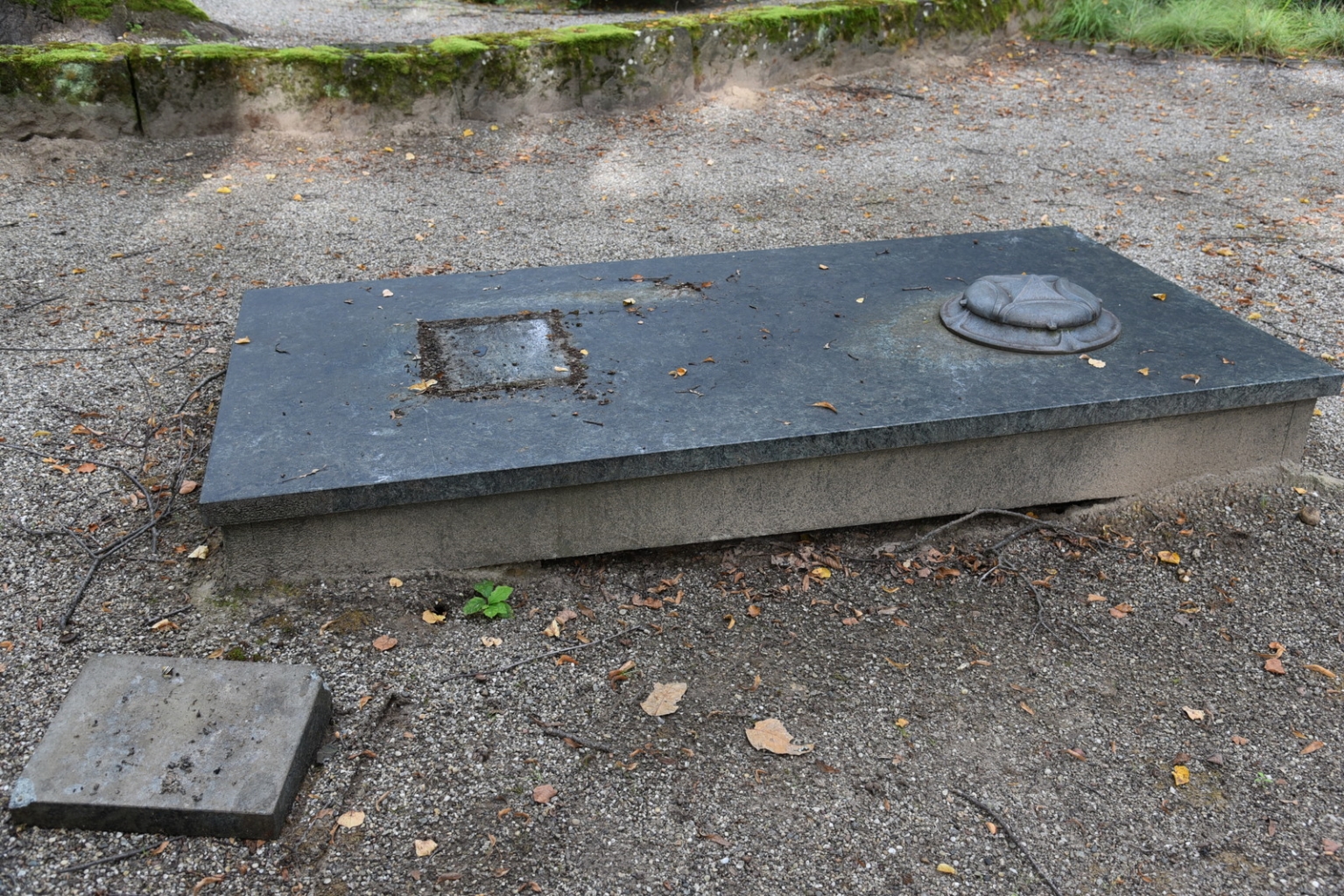 Ein umgetretener Grabstein auf dem Friedhof, der neben der Grabstelle liegt.